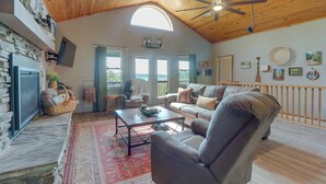 A spacious living area with a stone fireplace, leather sofas, a wooden ceiling, and a large window. - Beaver Lake Home w/ Game Room, Boat Slip & Views! (Eureka Springs)