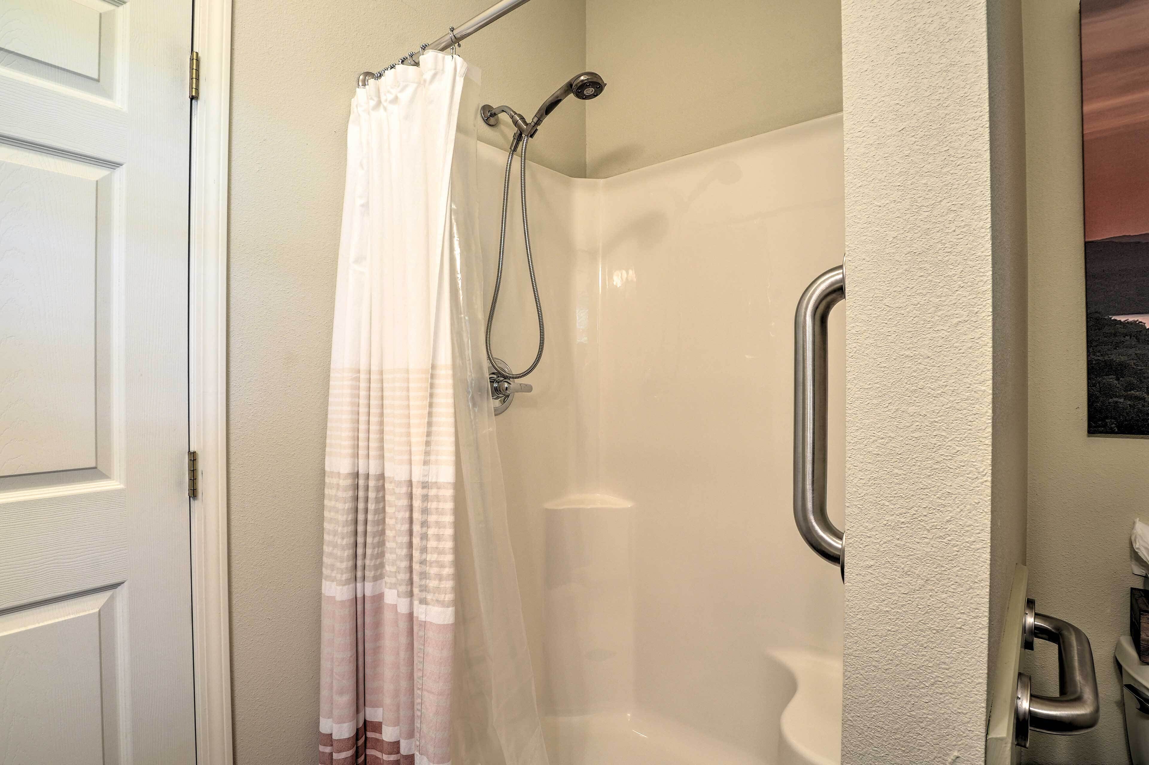 A shower with a glass door, a curtain, and a handrail.