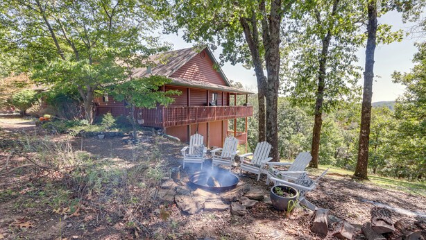 A cabin with a deck, surrounded by trees, and a fire pit with chairs. - Beaver Lake Home w/ Game Room, Boat Slip & Views! (Eureka Springs)