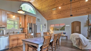 A spacious kitchen with wooden cabinets, a dining table with chairs, a large window, and a stone fireplace. - Beaver Lake Home w/ Game Room, Boat Slip & Views! (Eureka Springs)