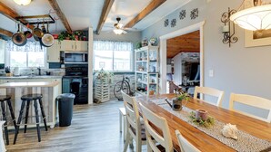Eine Küche mit Holzbalken, ein Essbereich mit Holztisch und Stühlen sowie ein Blick ins Wohnzimmer.