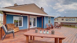 Eine Holzterrasse mit Tisch und Stühlen, ein überdachter Patio-Bereich und ein Haus mit blauer Außenverkleidung und einem braunen Dach.