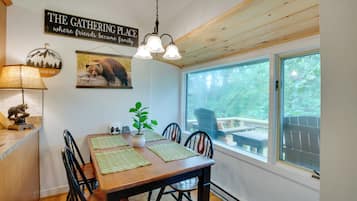 A dining area with a wooden table, chairs, a hanging light fixture, a wall sign, and a window with a view of the outdoors.