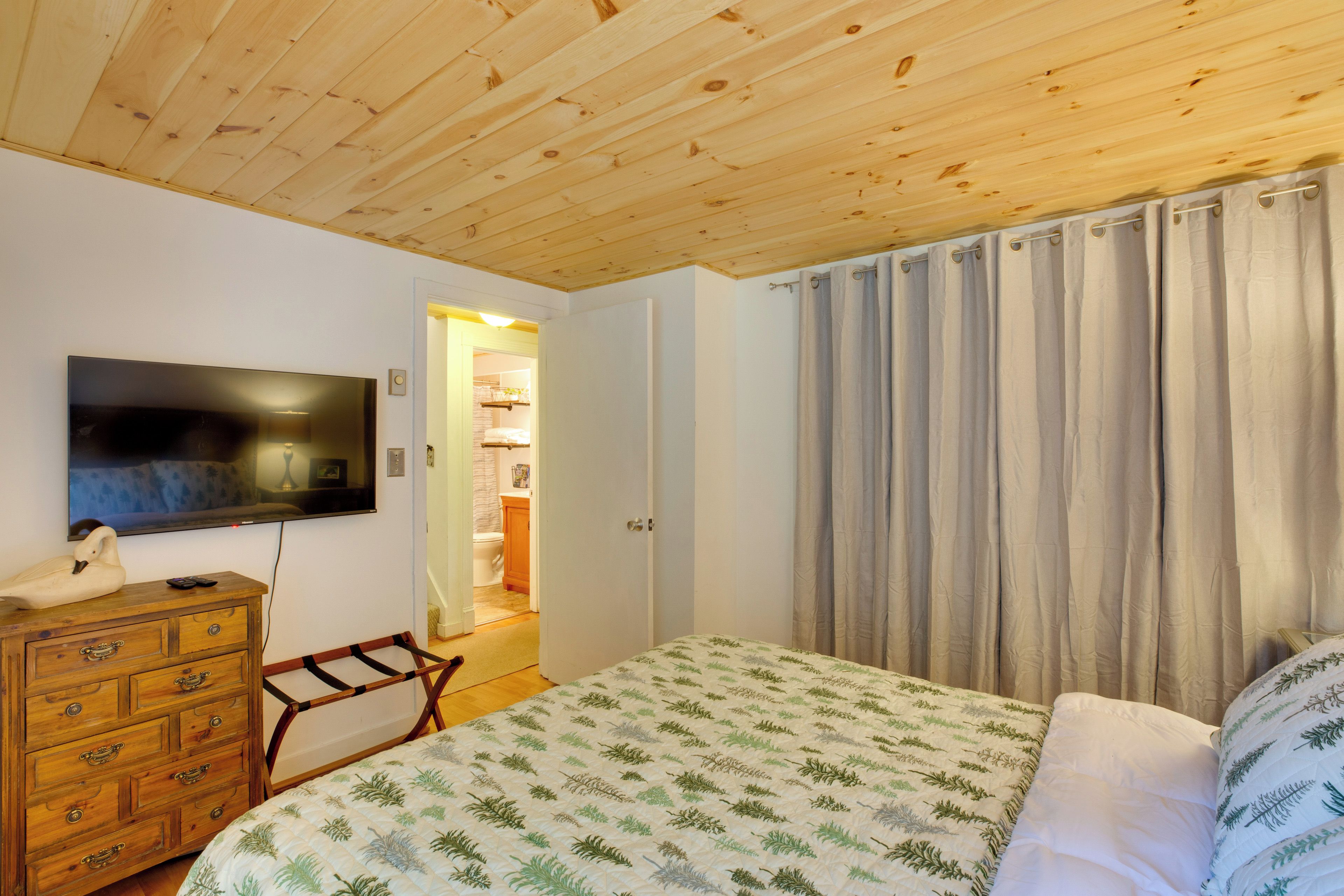 Ein Schlafzimmer mit Holzboden, einem Bett mit deckenmuster in Form von Blättern, einem Fernseher an der Wand und einer Holzkommode.