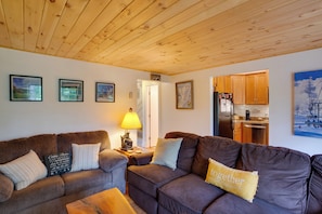 A cozy living room with a wooden ceiling, a sofa set, a coffee table, and a kitchen area visible through an open door. - Steps to Sugar Mountain! Condo w/ Furnished Deck (Banner Elk)