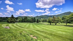 A well-maintained grassy field with trees and a mountain in the background.