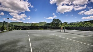 A tennis court with a net, surrounded by greenery and hills.