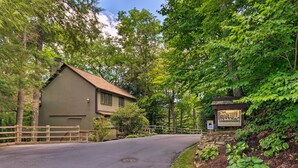 A wooden cabin with a metal roof, surrounded by lush greenery and a stone wall.