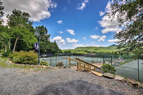 A tennis court with a wooden fence and a bench, surrounded by trees and hills. - Steps to Sugar Mountain! Condo w/ Furnished Deck (Banner Elk)