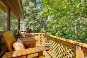 Une terrasse en bois avec une table et des chaises, entourée d’un feuillage dense.