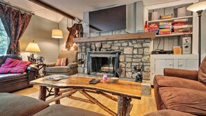 A cozy living room with a stone fireplace, a flat-screen TV mounted above it, and a bookshelf filled with books and board games.