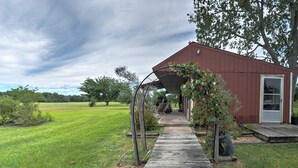 A rustic wooden structure with a covered walkway leading to a door, surrounded by a grassy field and trees. - Delightful Carmine Studio on Rocking Horse Farm! (Carmine)