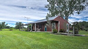 A single-story house with a red exterior, a covered porch, and a large tree in front. - Delightful Carmine Studio on Rocking Horse Farm! (Carmine)