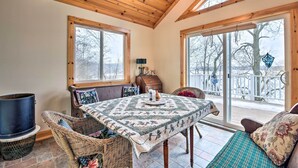 A cozy room with a wooden ceiling, large windows, a table with a quilt, wicker chairs, and a view of a snowy landscape.