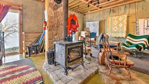 A rustic interior with a stone wall, a wooden stove, a rocking chair, and a colorful rug.