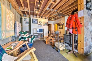 Quarto aconchegante com vigas de madeira aparentes, televisão, lareira e uma variedade de colchas e mantas.