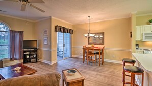 A spacious living area with a television, sofa, coffee table, and a dining area with chairs and a chandelier. - Golfer's Paradise: Myrtle Beach Condo w/ Pool! (Myrtle Beach)