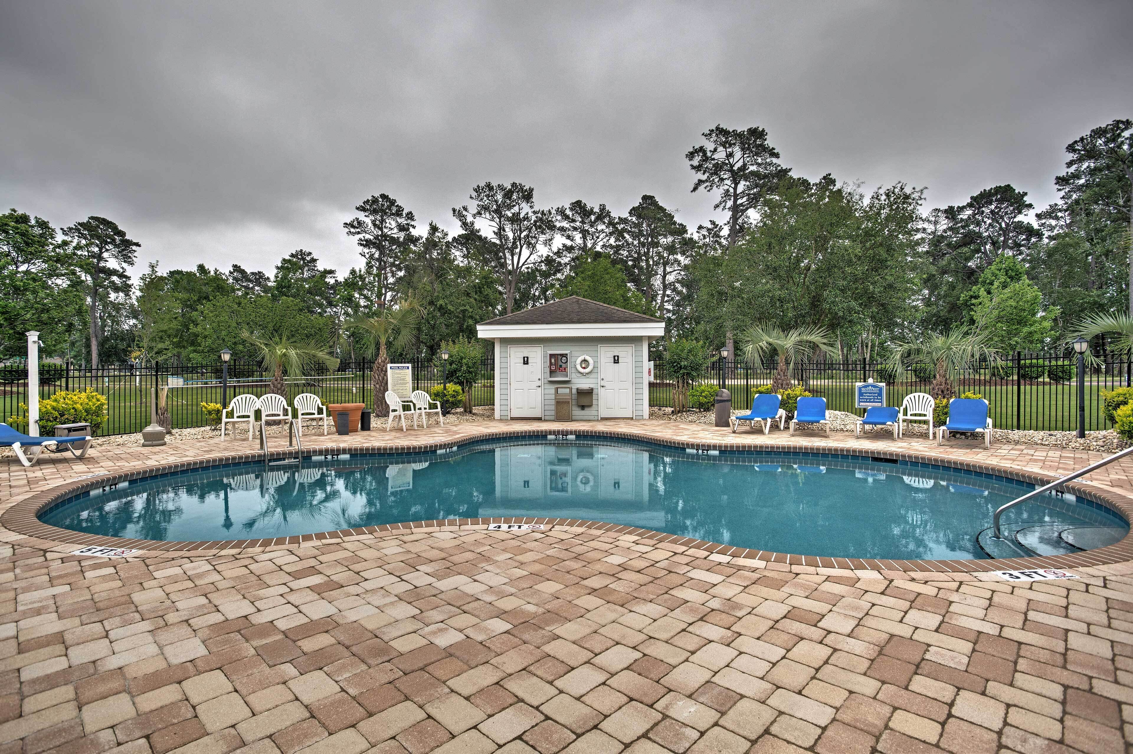 A swimming pool with a small building, lounge chairs, and a brick patio.