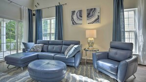 A modern living room with a sectional sofa, a chaise lounge, and a side table with a lamp. There are two large windows with curtains, and abstract art on the wall. - Modern Durham Retreat w/ Private Yard & Patio (Durham)