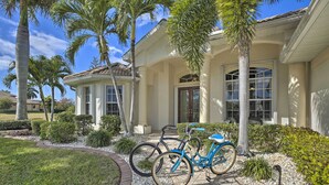 A residential house with a driveway, two bicycles, and a well-maintained garden with palm trees and shrubs. - Waterfront Cape Coral Home w/ Private Dock & Lanai (Cape Coral)
