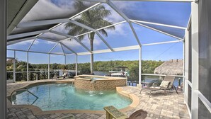 A covered outdoor swimming pool with lounge chairs and a thatched-roof structure. - Waterfront Cape Coral Home w/ Private Dock & Lanai (Cape Coral)