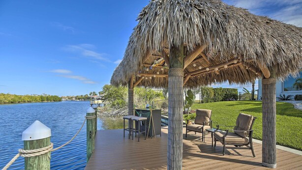 A wooden deck with a thatched gazebo, outdoor furniture, and a view of the water. - Waterfront Cape Coral Home w/ Private Dock & Lanai (Cape Coral)