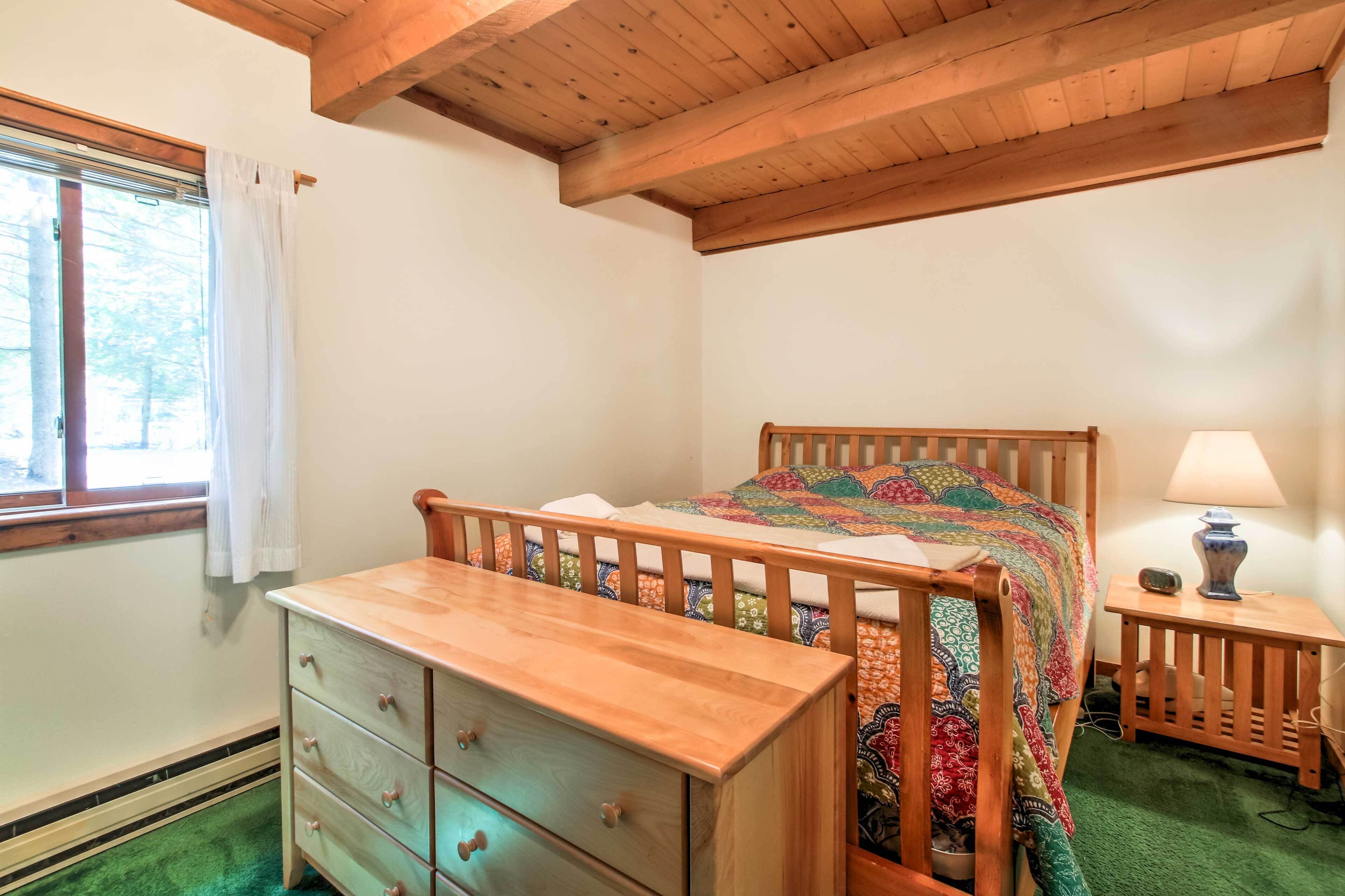 Een slaapkamer met een houten bed, een dressoir, een nachtkastje en een raam met gordijnen.