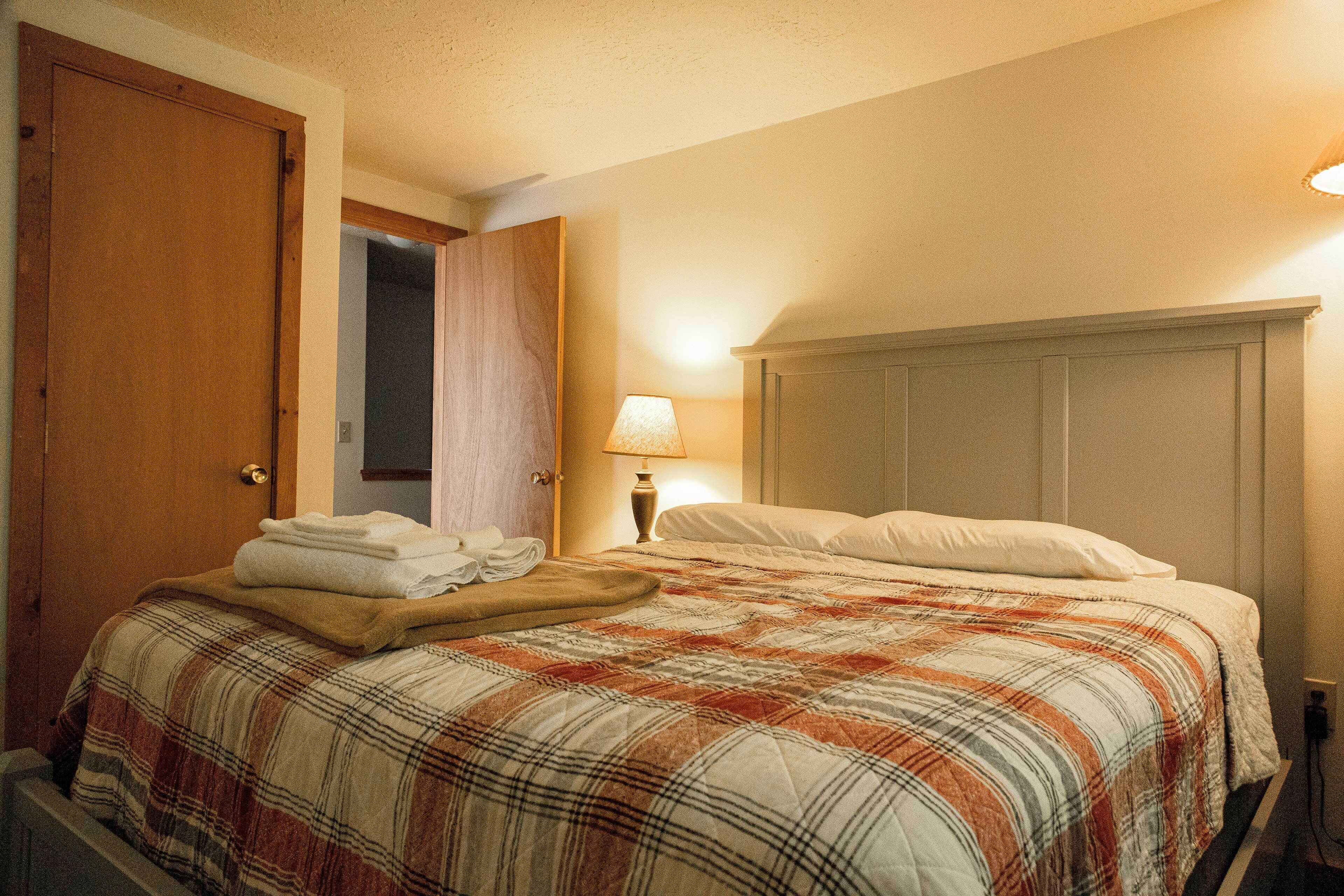 Una habitación de hotel con una cama, una mesita de noche, una lámpara y una puerta.