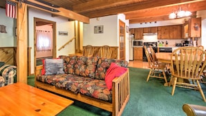A cozy living area with a sofa, wooden dining table, and chairs. A kitchen with wooden cabinets and appliances is visible in the background. - Cozy Bartlett Townhome < 3 Mi to Attitash Mountain (Bartlett)