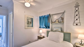 A bedroom with a bed, a nightstand, a lamp, a ceiling fan, a window with curtains, and a wall-mounted shelf with decorative items. - Ormond Beach Retreat w/ Deck - Steps to Ocean! (Ormond Beach)