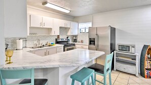 A modern kitchen with white cabinetry, a marble island, and a built-in microwave. - Ormond Beach Retreat w/ Deck - Steps to Ocean! (Ormond Beach)