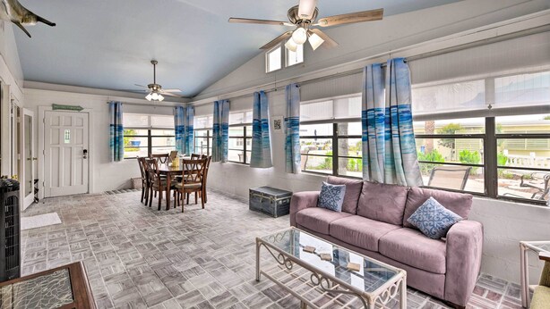 A spacious living room with a high ceiling, ceiling fans, a pink sofa, a glass coffee table, and a dining area with a table and chairs. - Ormond Beach Retreat w/ Deck - Steps to Ocean! (Ormond Beach)
