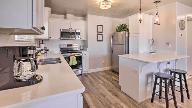 A modern kitchen with white cabinetry, stainless steel appliances, and a central island with stools. - Central Kanab Apartment w/ Updated Interior! (Kanab)