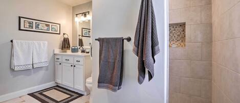 A bathroom with a toilet, sink, and shower. There are towels on the wall and a rug on the floor.