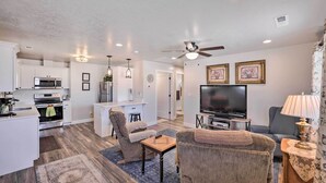 A modern kitchen with white cabinets, a microwave, and an oven. There is a dining area with a table and chairs, a living room with a sofa and a TV, and a ceiling fan. - Central Kanab Apartment w/ Updated Interior! (Kanab)