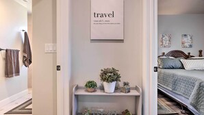 A hallway with a sign that reads "travel" and a definition, a bed with a patterned bedspread, and a wall with two framed floral signs. - Central Kanab Apartment w/ Updated Interior! (Kanab)