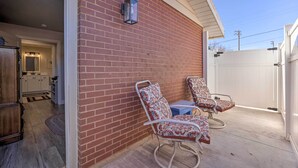 A patio with two rocking chairs and a small table, a brick wall, and a white fence. - Central Kanab Apartment w/ Updated Interior! (Kanab)