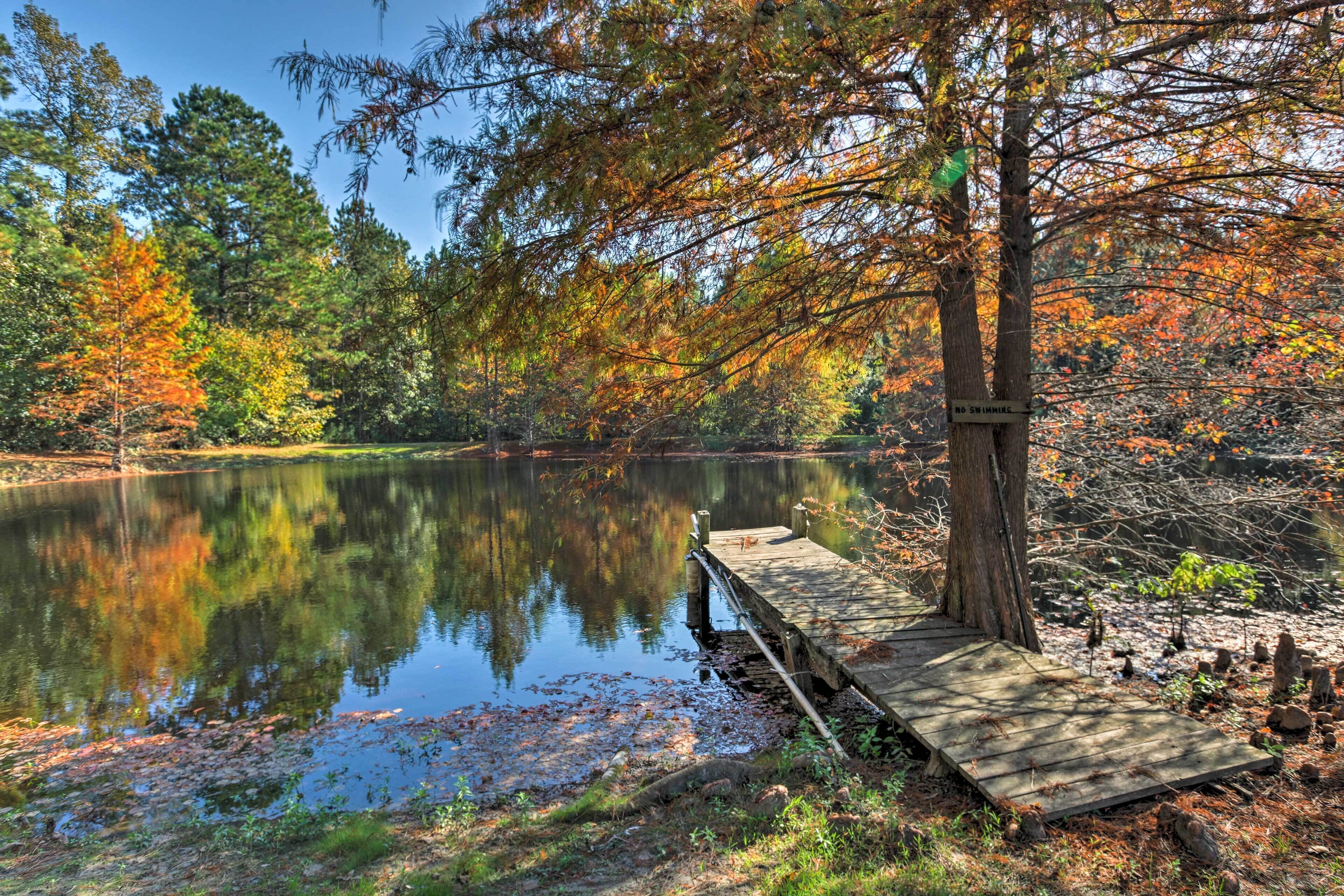 A wooden dock extending into a calm lake surrounded by trees with autumn foliage.