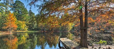 A wooden dock extending into a calm lake surrounded by trees with autumn foliage.