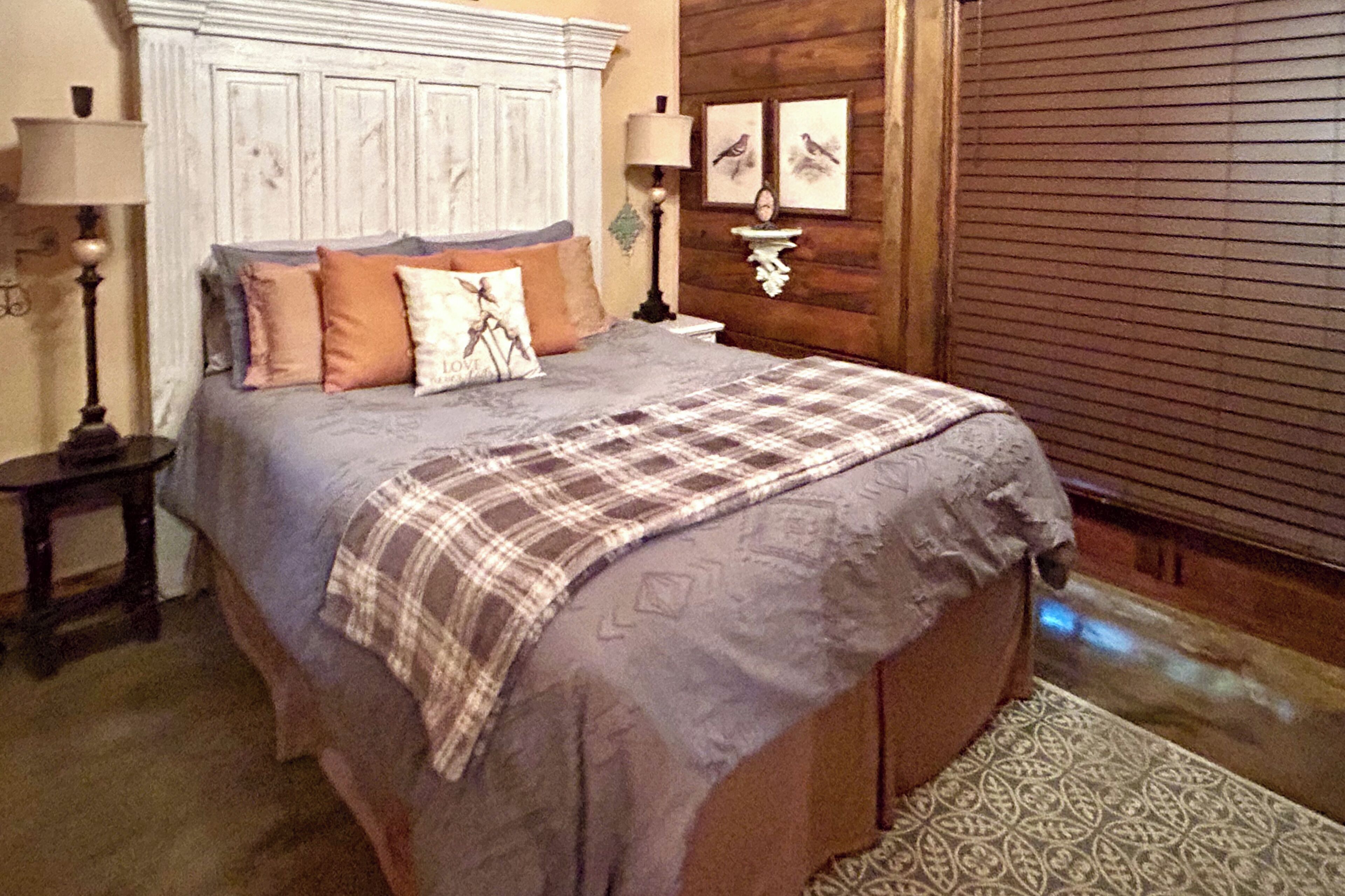 A bedroom with a bed, two bedside tables, a lamp, and a wall-mounted shelf with pictures.
