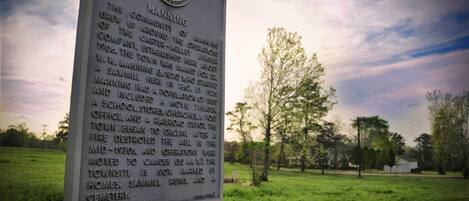 A historical marker in a grassy area with trees and a cloudy sky in the background.
