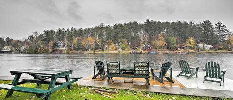 A lakeside picnic area with a table and chairs, surrounded by trees and houses.