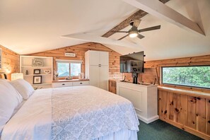 A bedroom with a large bed, a ceiling fan, wooden walls, a window, and a kitchenette area. - 'skylight' Adirondack Cabin w/ On-site Lake (Saranac Lake)