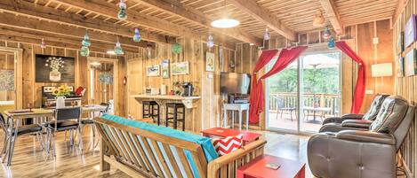 A spacious living area with a wooden ceiling, a dining table with chairs, a sofa, a red table, and a leather recliner.
