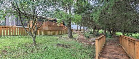 Eine Holzterrasse führt zu einem umzäunten Garten mit einer weiteren Holzterrasse und einem Haus im Hintergrund.