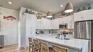 A modern kitchen with white cabinets, a large island, hanging pendant lights, and a stainless steel refrigerator. - 6 Mi to Beach: Rockport Home w/ Pool Access! (Rockport)