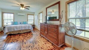 A bedroom with a bed, dresser, ceiling fan, and large windows.