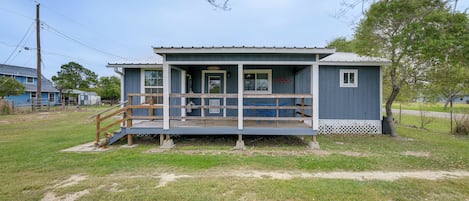 A small, single-story building with a porch, a staircase, and a fenced yard.