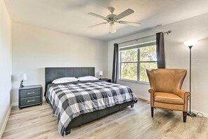 A bedroom with a bed, a nightstand, a chair, a ceiling fan, and a window with curtains.