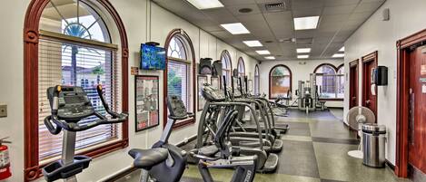 A gym with multiple treadmills and exercise equipment, large windows with blinds, and a checkered floor.